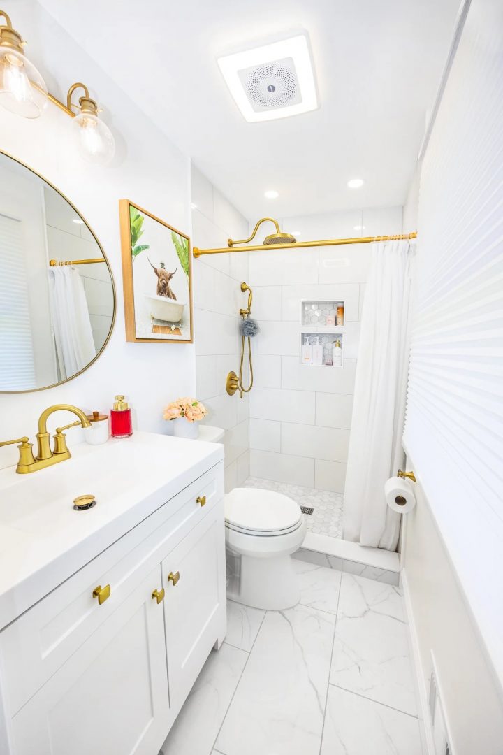 Custom white vanity with quartz top, gold faucet, and round mirror in Rochester NY bathroom remodel.