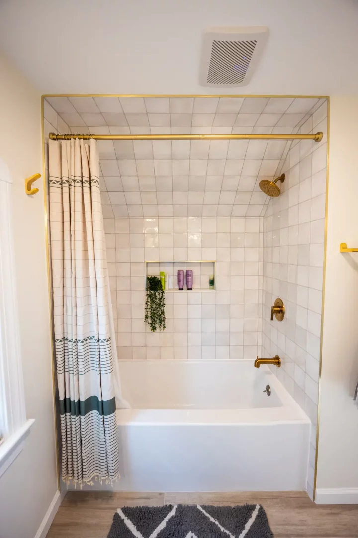 Tiled shower with built-in niche and gold fixtures in Rochester bathroom.